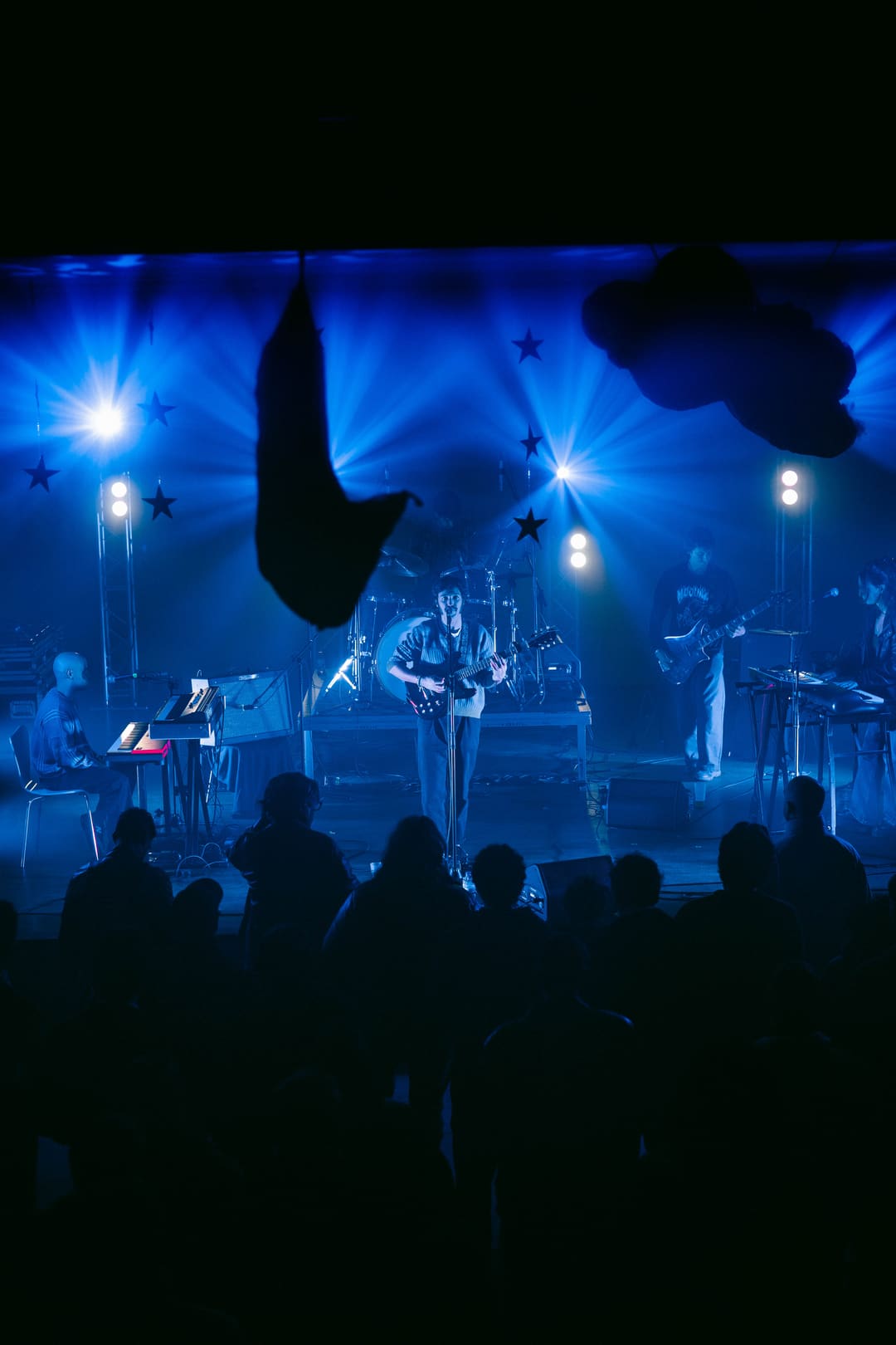 Banda em palco sob luzes azuis, vista da plateia, num concerto do FEN Winter Sessions